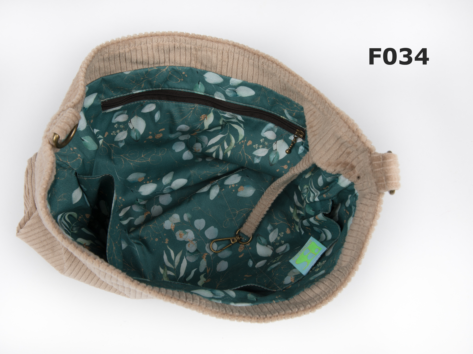 Geöffnete Cordtasche mit petrolfarbenem Eukalyptusblätterfutter, Innenfächern und Schlüsselband.