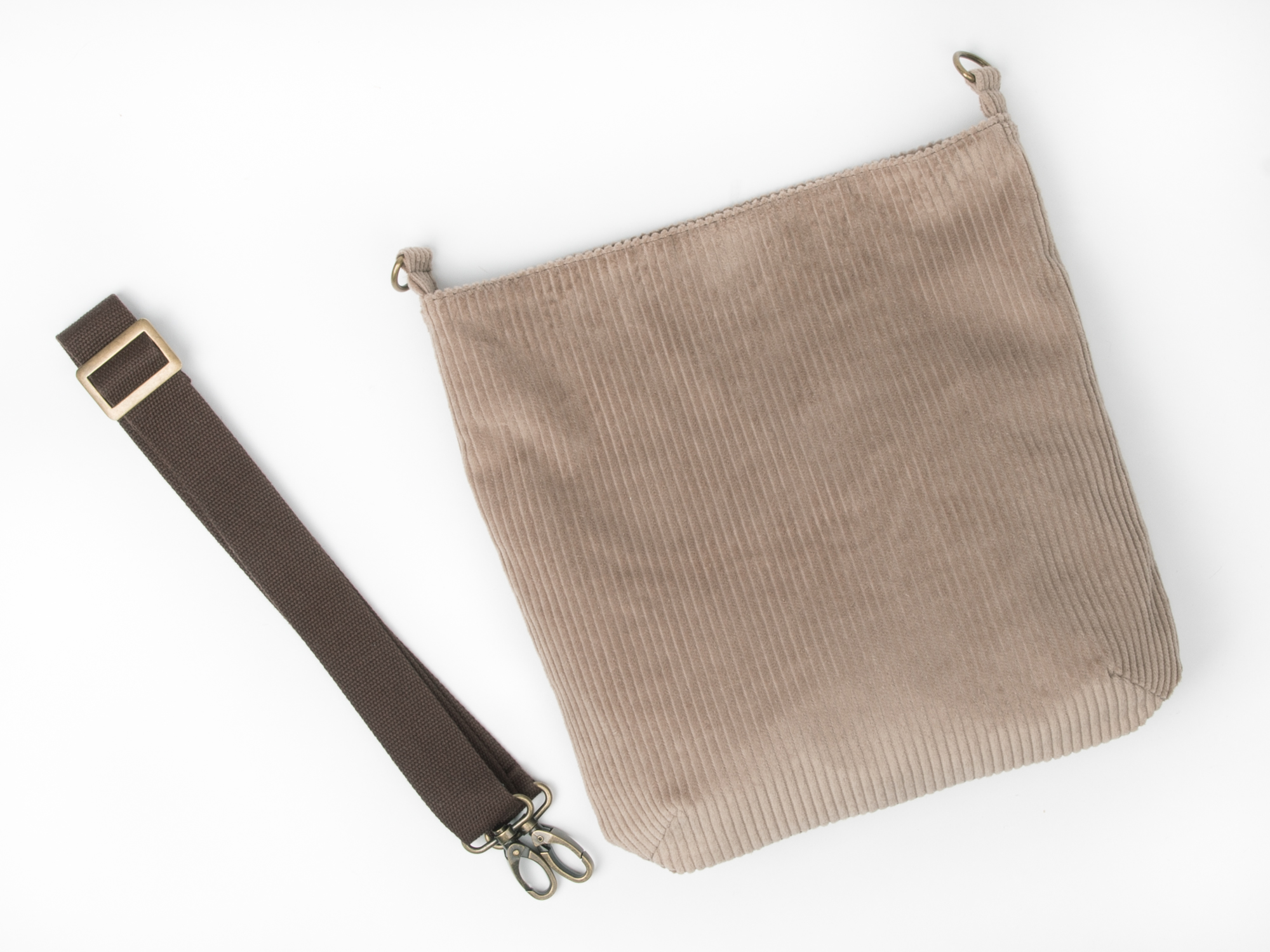 Taupefarbene Cordtasche neben ihrem abgenommenen braunen Schultergurt.